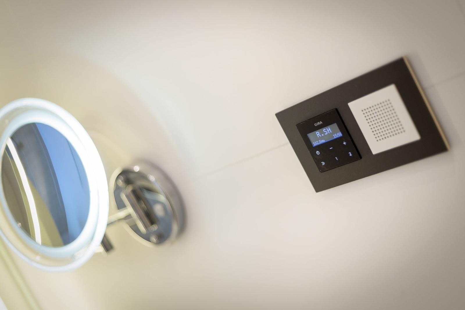 Wall-mounted control with display and speaker next to a lit mirror.