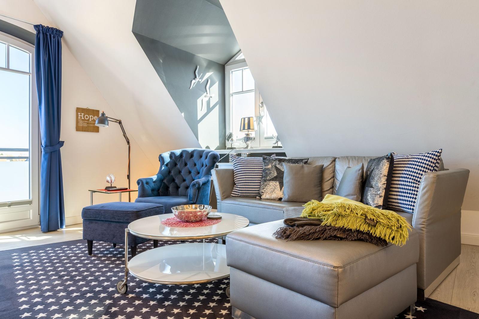 Living room with sofa, armchair, and table under sloped ceiling.
