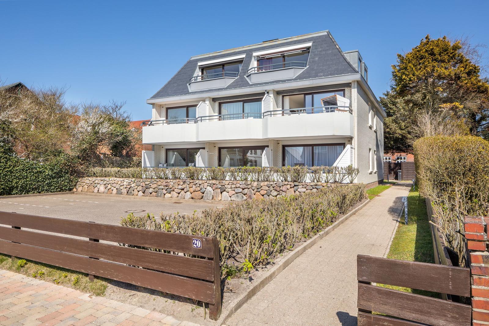 Modern multi-family house with balconies and stone wall. Access via walkway.
