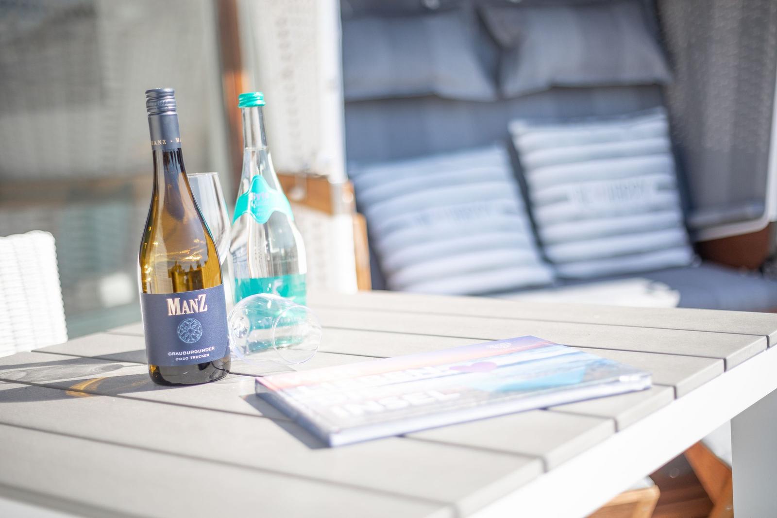 Table with wine bottle, water, and brochure on an outdoor terrace.