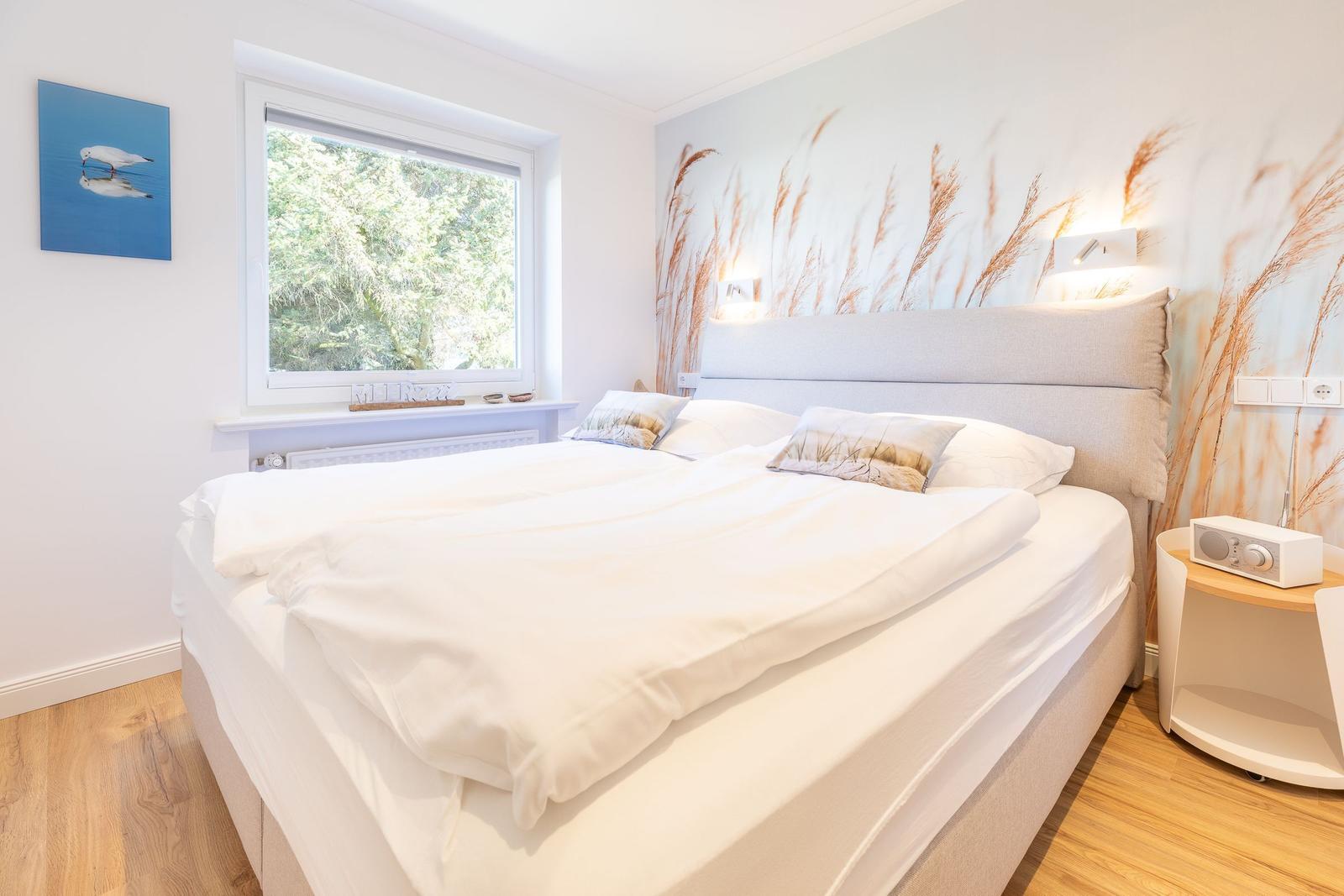 Bedroom with large bed, window and wall mural of reeds.