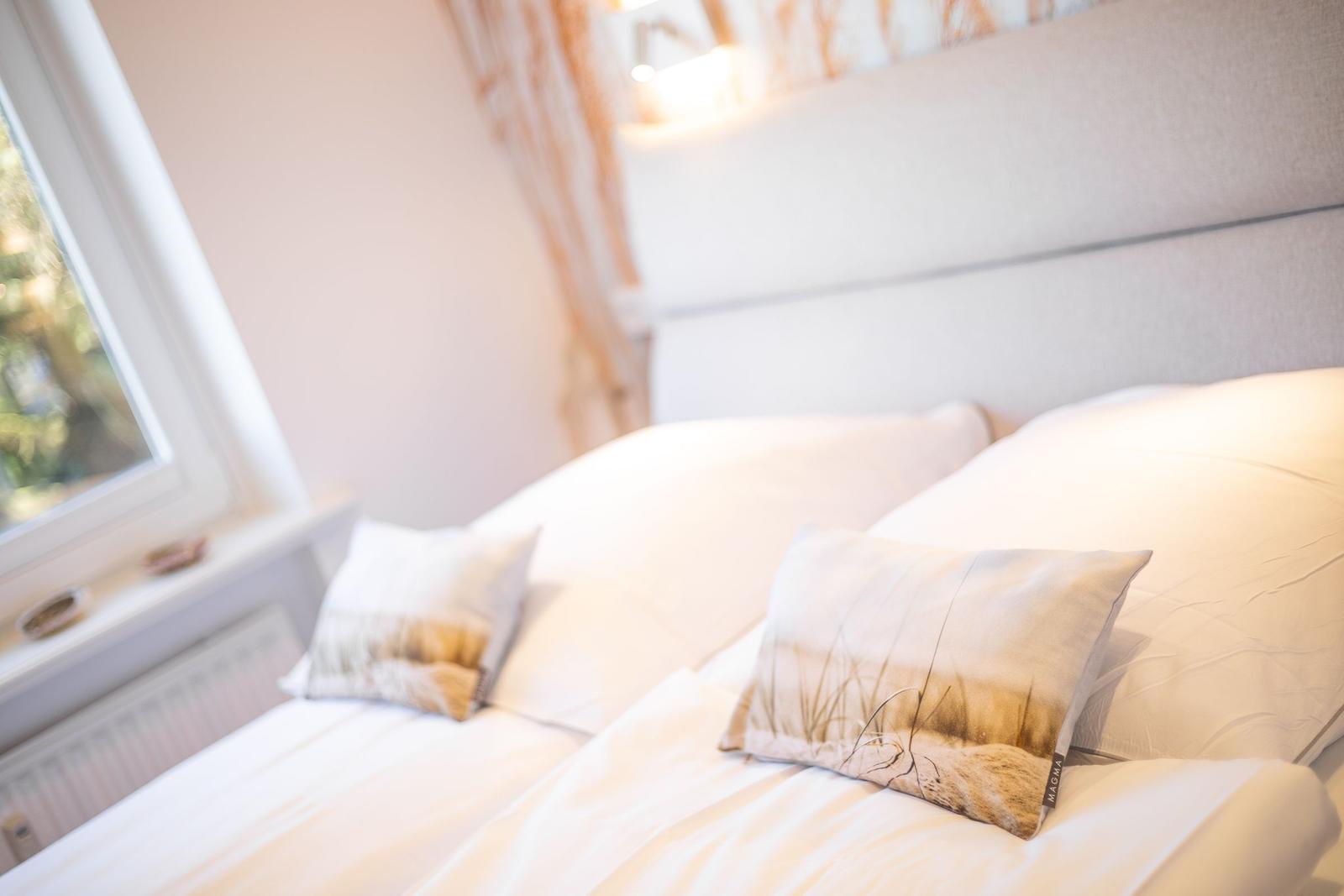 A bed with white sheets and pillows, a window, and a headboard.