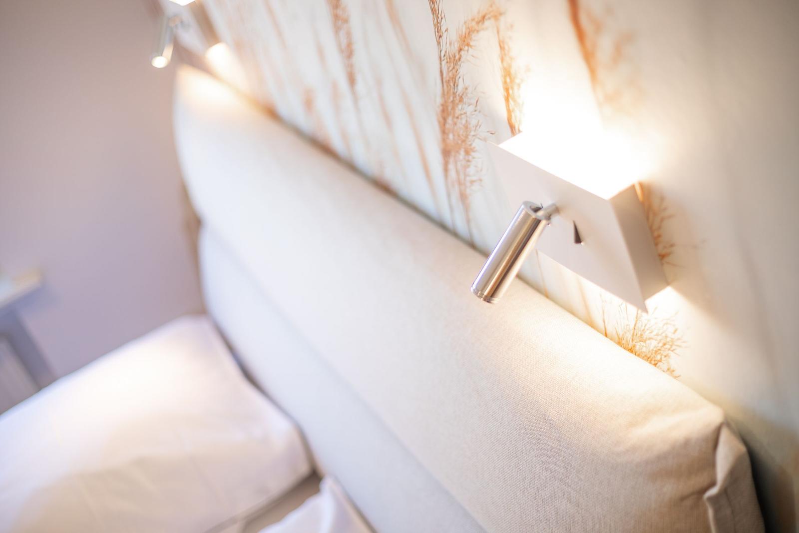 Bed headboard with modern wall lamp and decorative wallpaper.