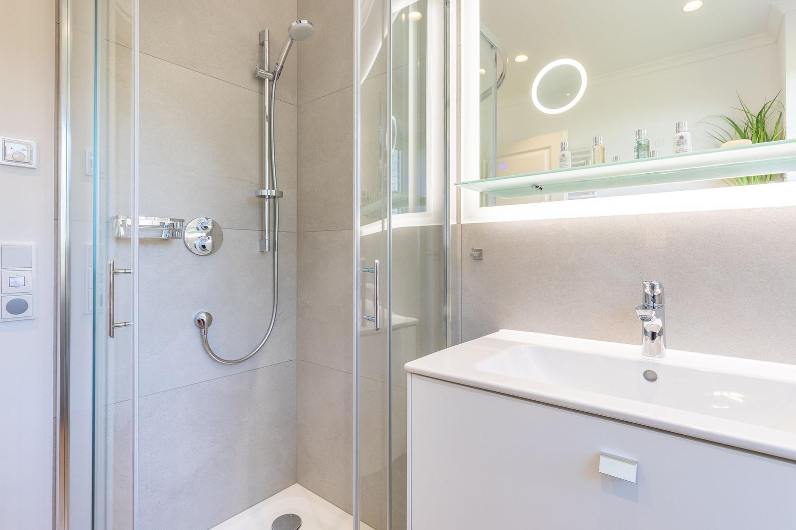 Shower with glass enclosure, sink and lit mirror