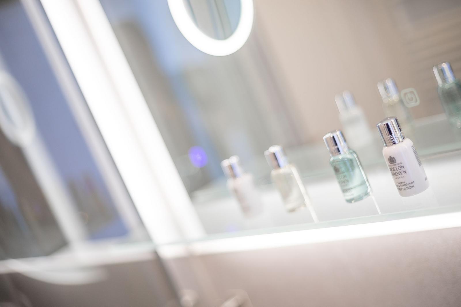Mirror with illuminated frame and bottles on glass shelf