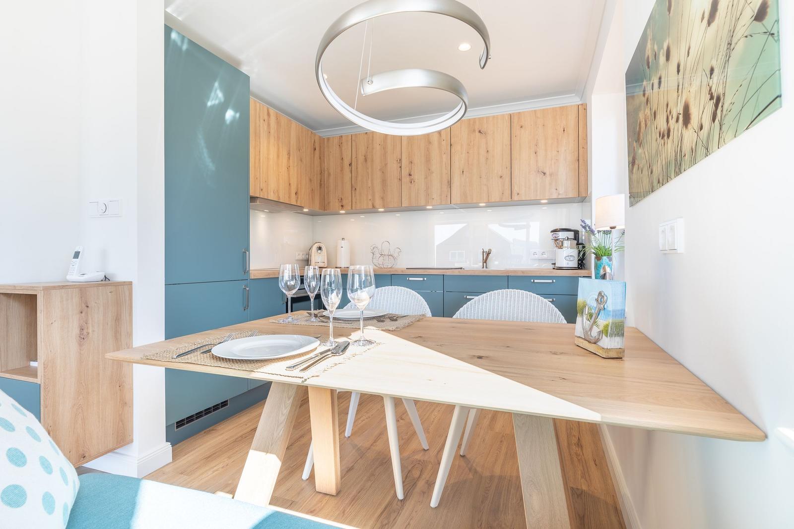 Dining area with wooden table and chairs. Kitchen with wooden cabinets and blue fronts.