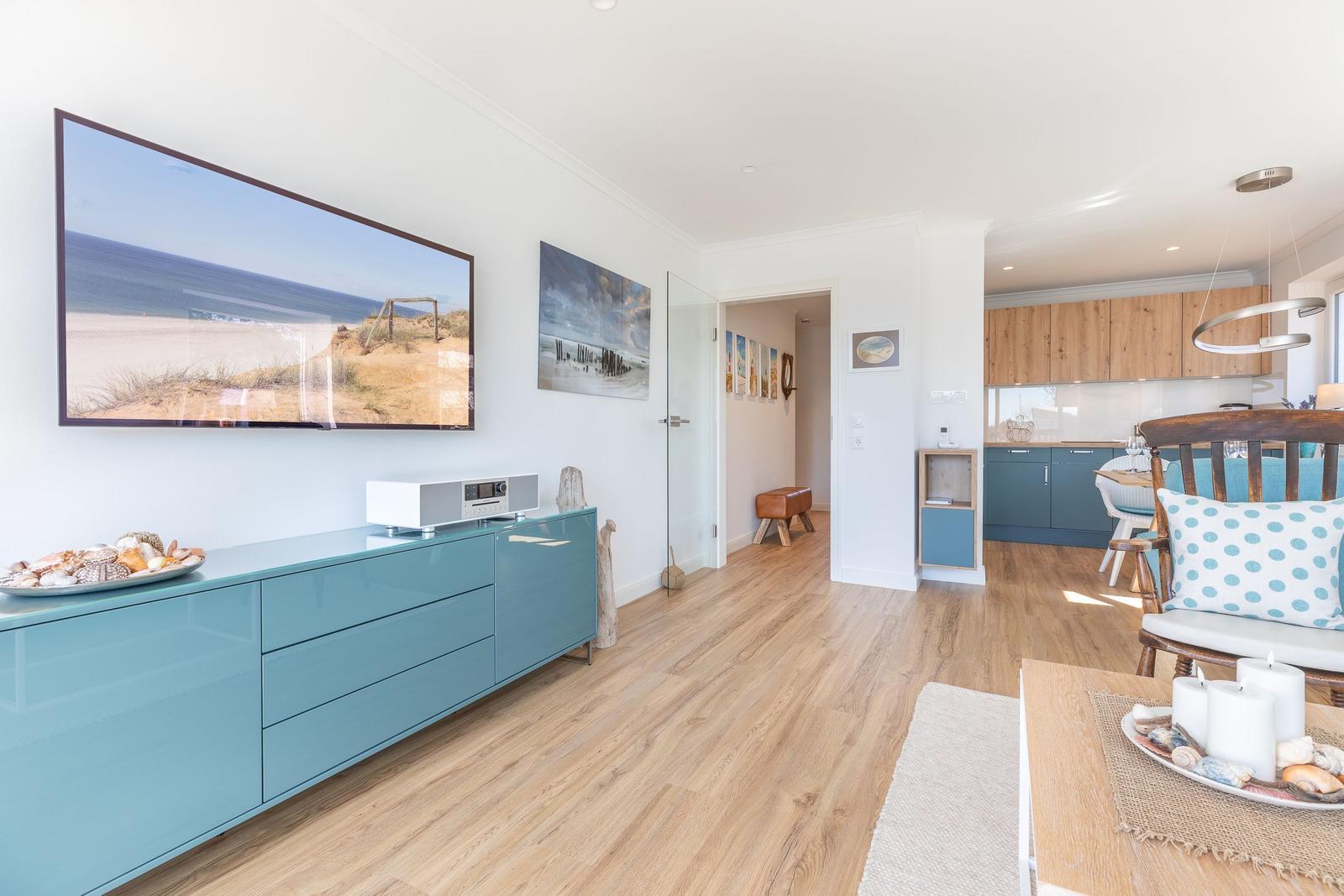 Living area with kitchen area, wooden floor, and sea view pictures on the wall.