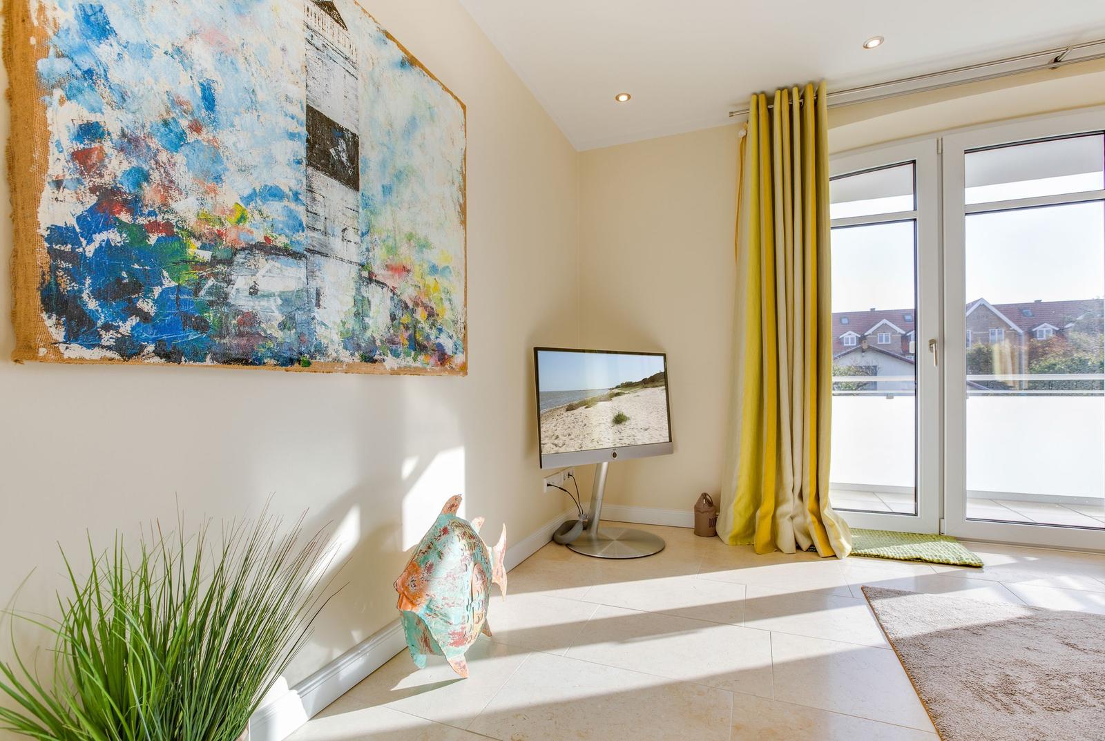 Raum mit Fernseher, großer Wanddekoration und Balkontür mit gelben Vorhängen.