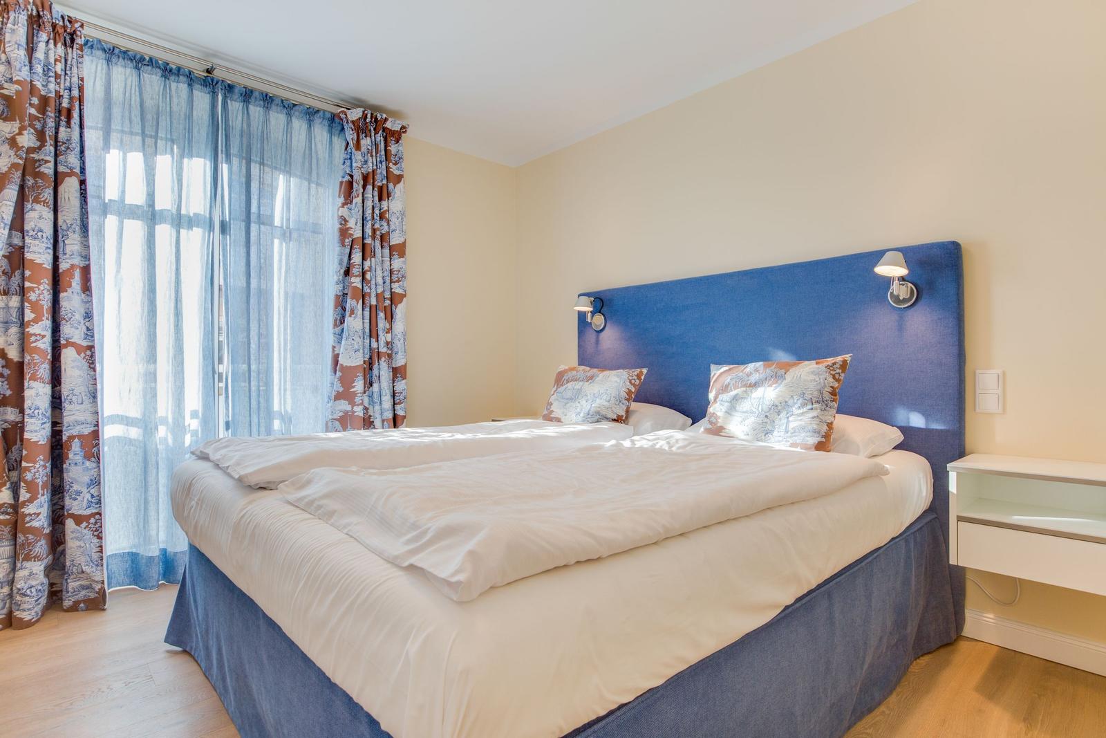 Schlafzimmer mit Doppelbett, blauem Kopfteil und Vorhängen mit Muster.