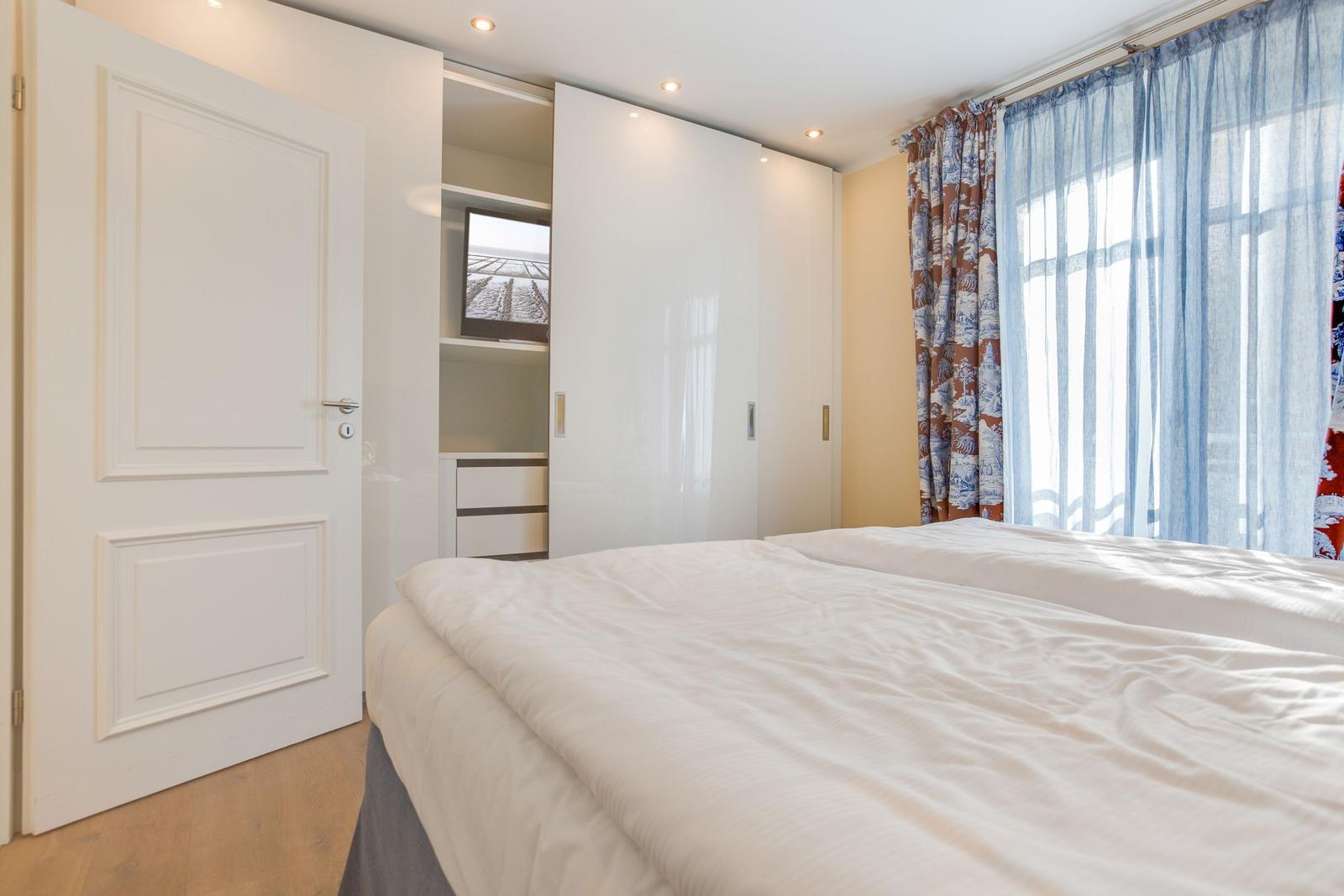 Schlafzimmer mit Doppelbett, Kleiderschrank und Fenster mit Vorhängen.
