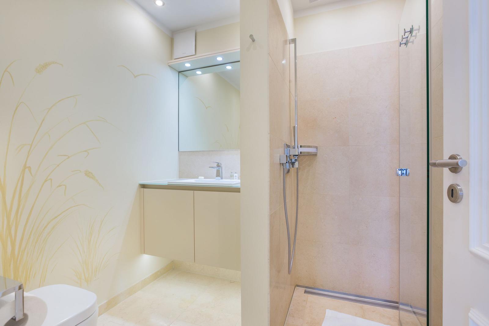 Badezimmer mit Dusche, Waschbecken und Toilette. Wandbild mit Pflanzenmotiv.
