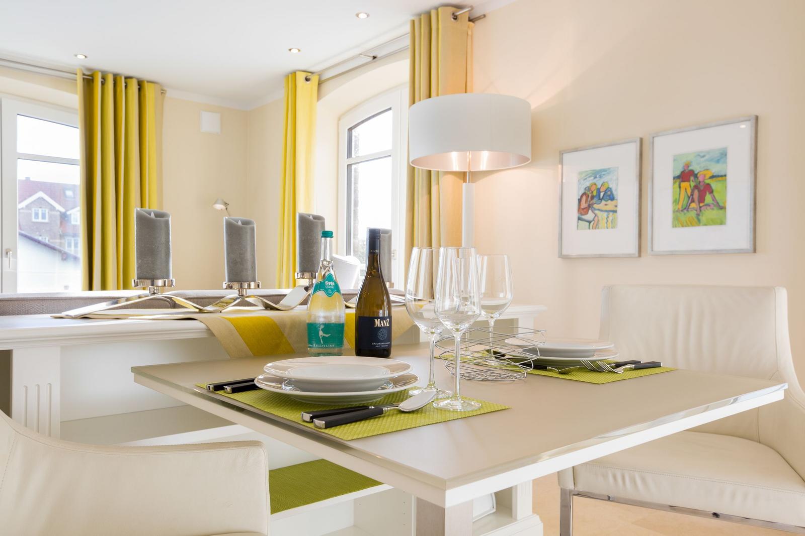 Esstisch mit Platz für vier Personen, gelbe Vorhänge und Bilder an der Wand.