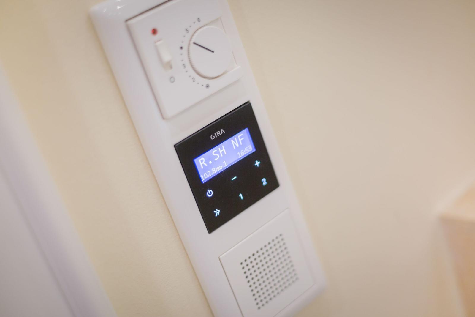 Wandmontierte Steuerung mit Temperaturregler und Digitaldisplay für Radio und Uhrzeit.