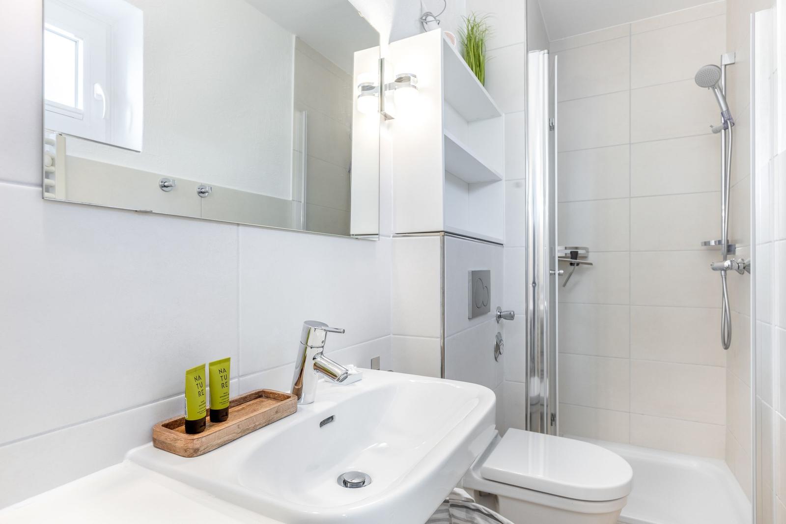 Badezimmer mit Waschbecken, Spiegel, Dusche und Toilette.