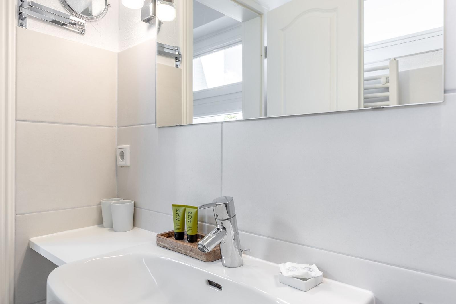 Badezimmer mit Waschbecken, Spiegel und Pflegeprodukten.