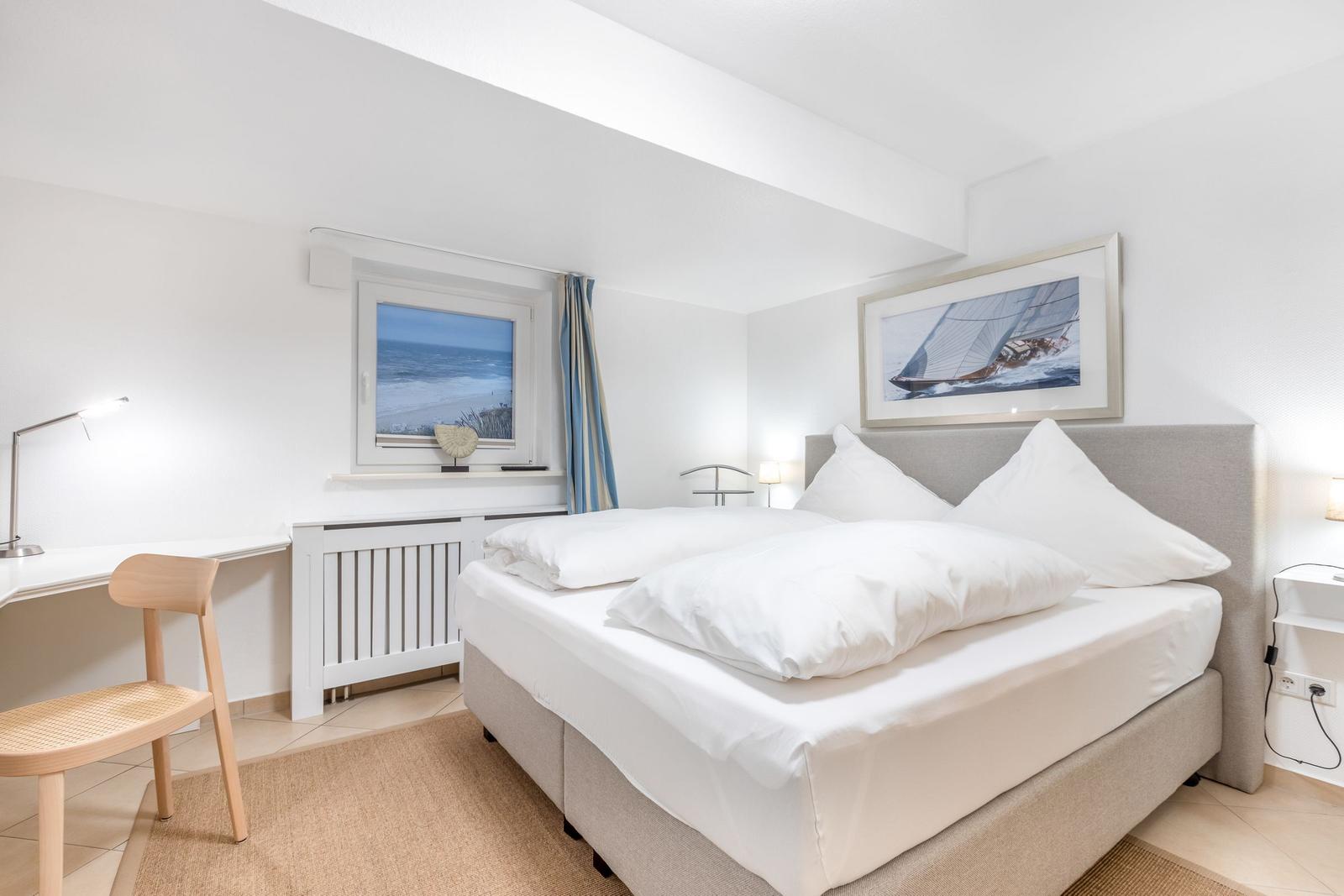 Schlafzimmer mit Bett, Schreibtisch und Meerblickfenster.