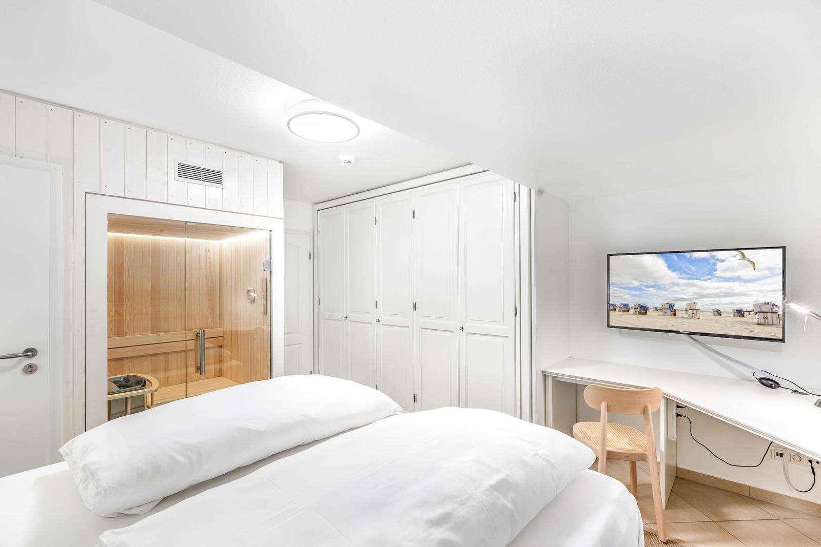 Schlafzimmer mit Doppelbett, Sauna, Kleiderschrank und Schreibtisch mit TV.