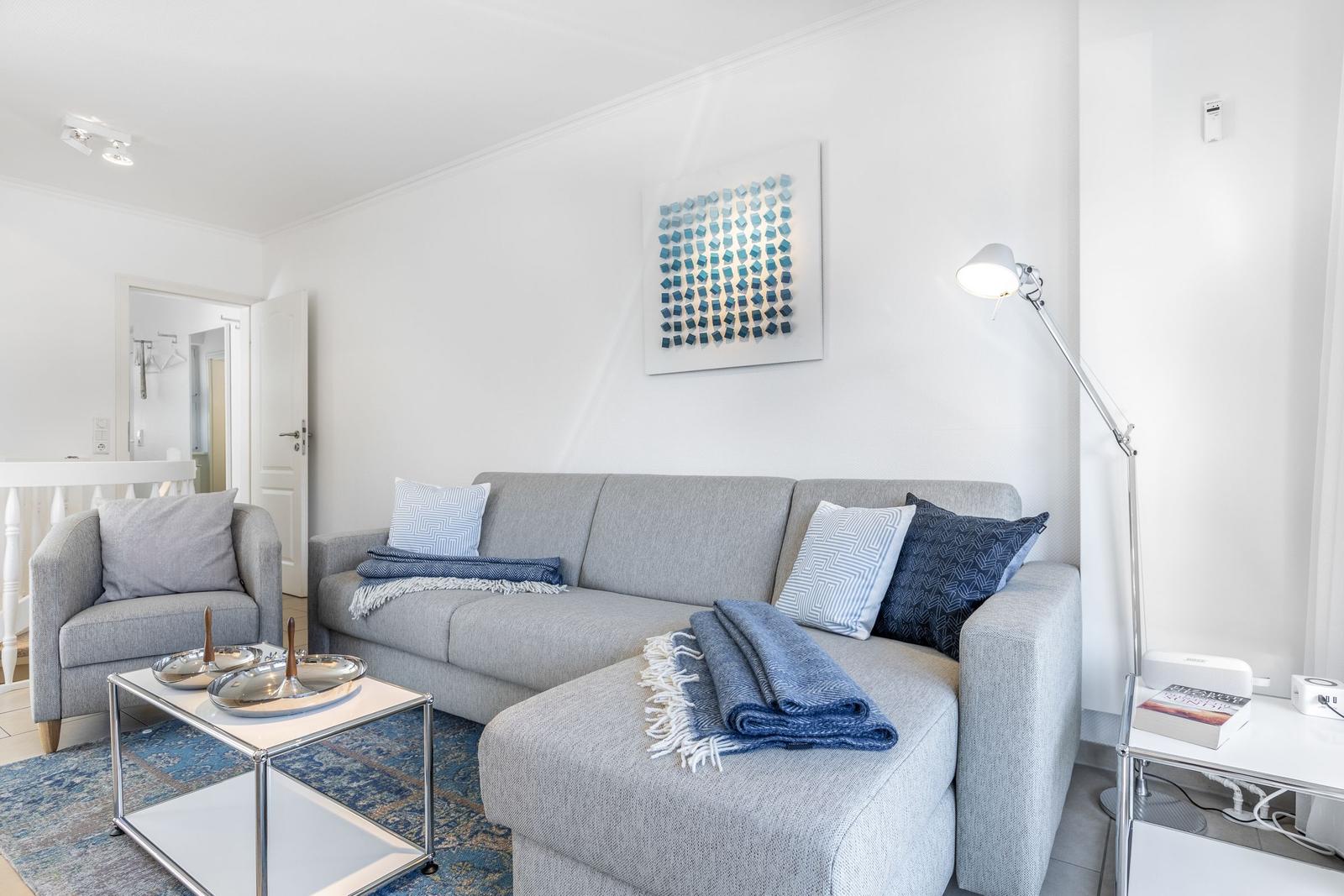 Wohnzimmer mit grauem Sofa, blauem Teppich und Stehlampe.