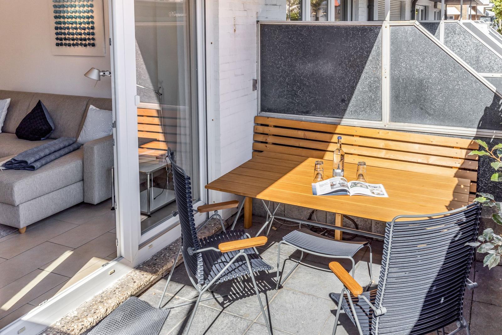 Terrasse mit Tisch, zwei Stühlen und Holzbank. Durchgang ins Wohnzimmer mit Sofa.