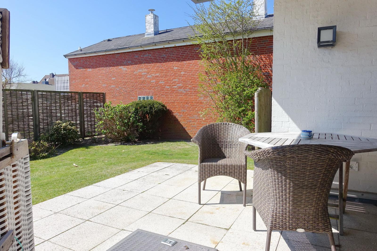 Terrace with table and chairs, lawn area, and red brick wall in the background.