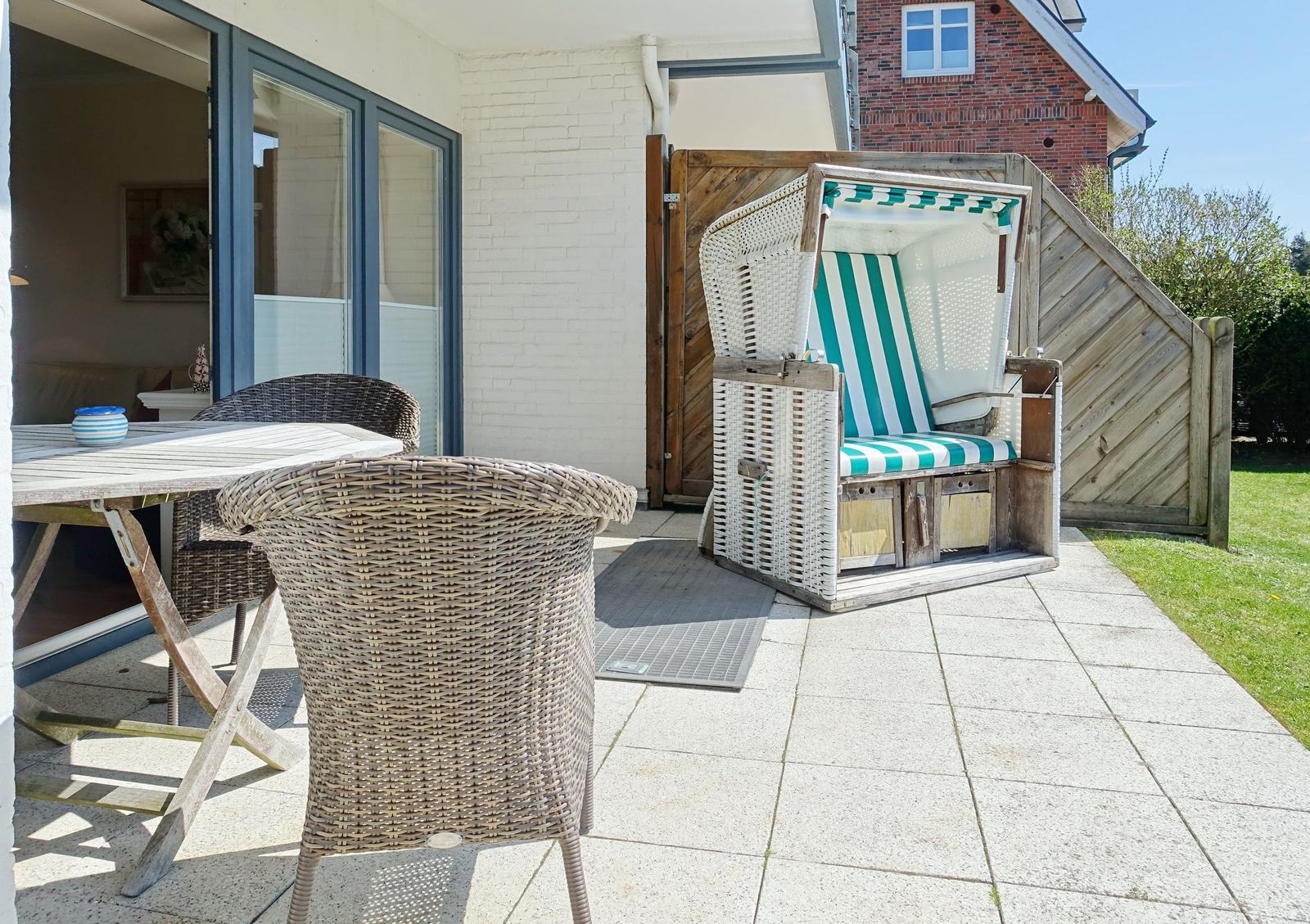 Terrace with dining table, chairs, and beach chair. Background: white plaster and wooden fence.