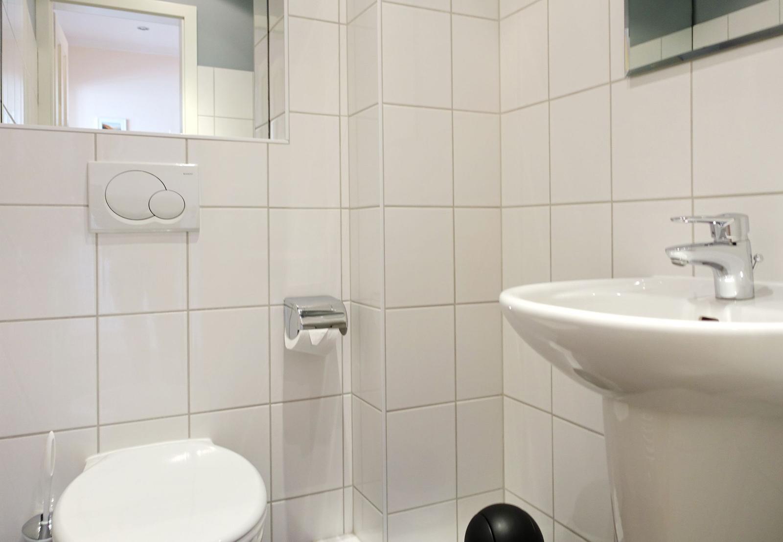 Bathroom with toilet, sink, and mirror on white tiled walls.