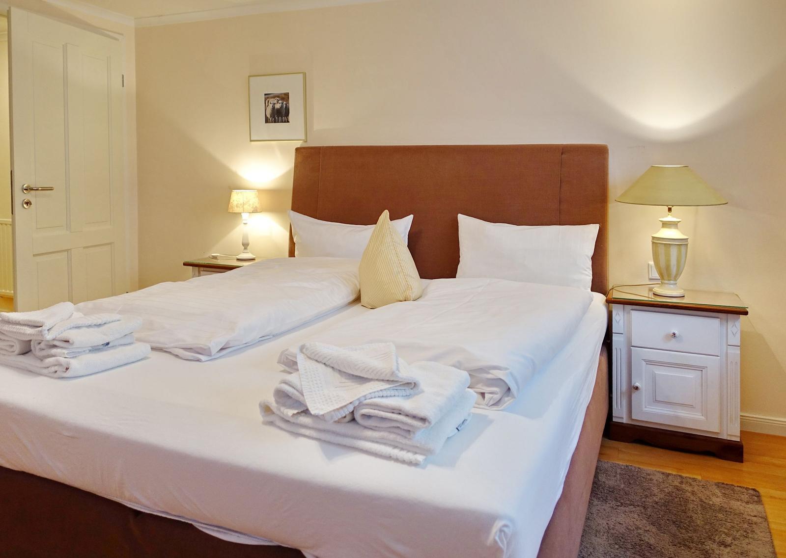 Bedroom with bed, nightstands, and lamps. Towels and bedding are ready.