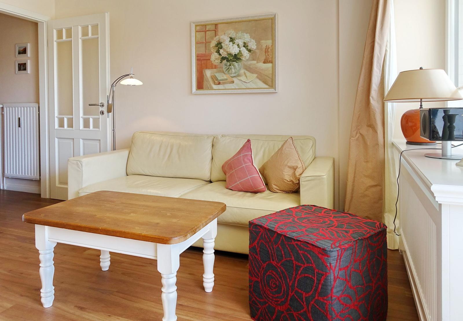 Living room with cream sofa, wooden table, and patterned ottoman.