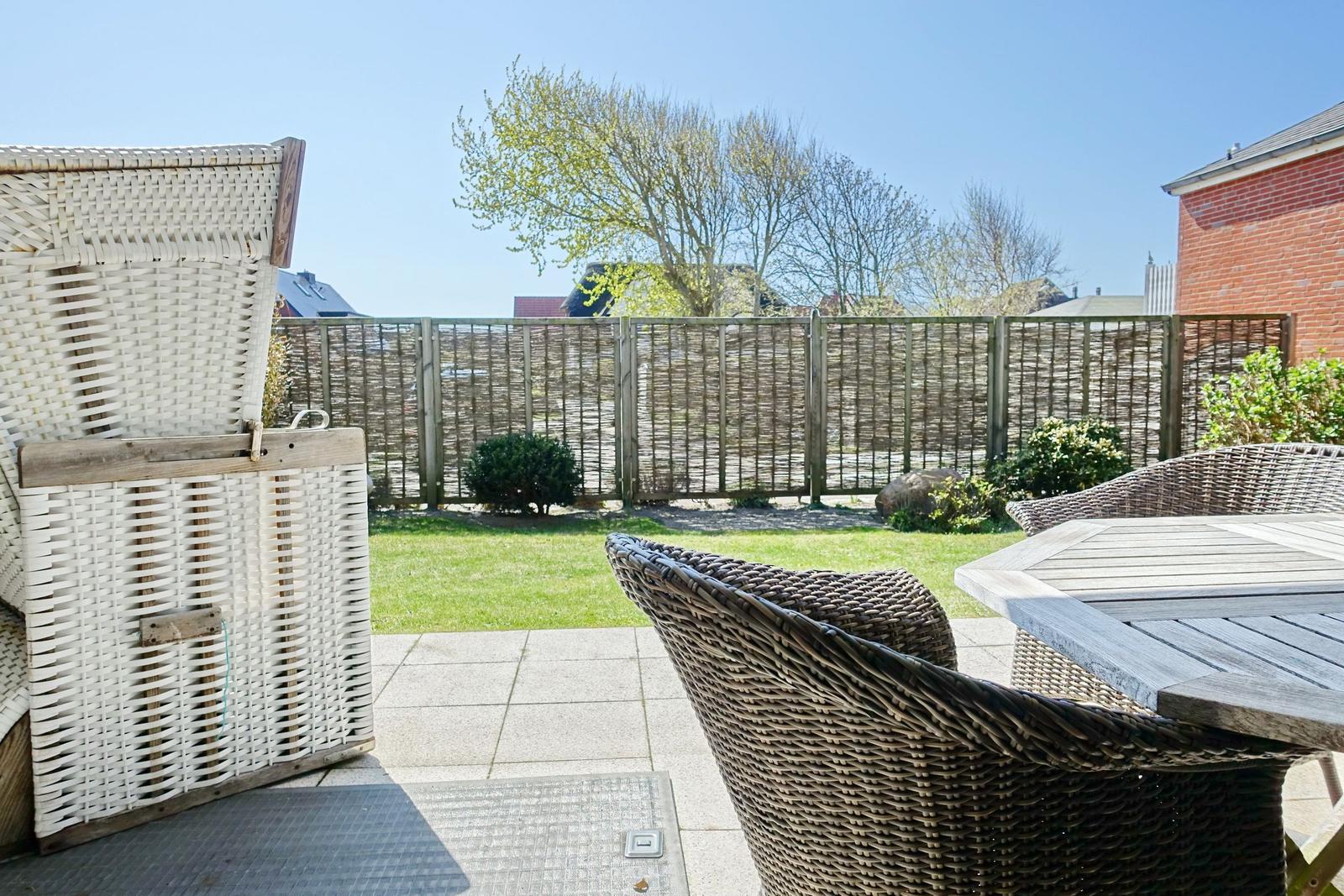 Terrace with wicker chairs and table. Backyard with grass and wooden fence.
