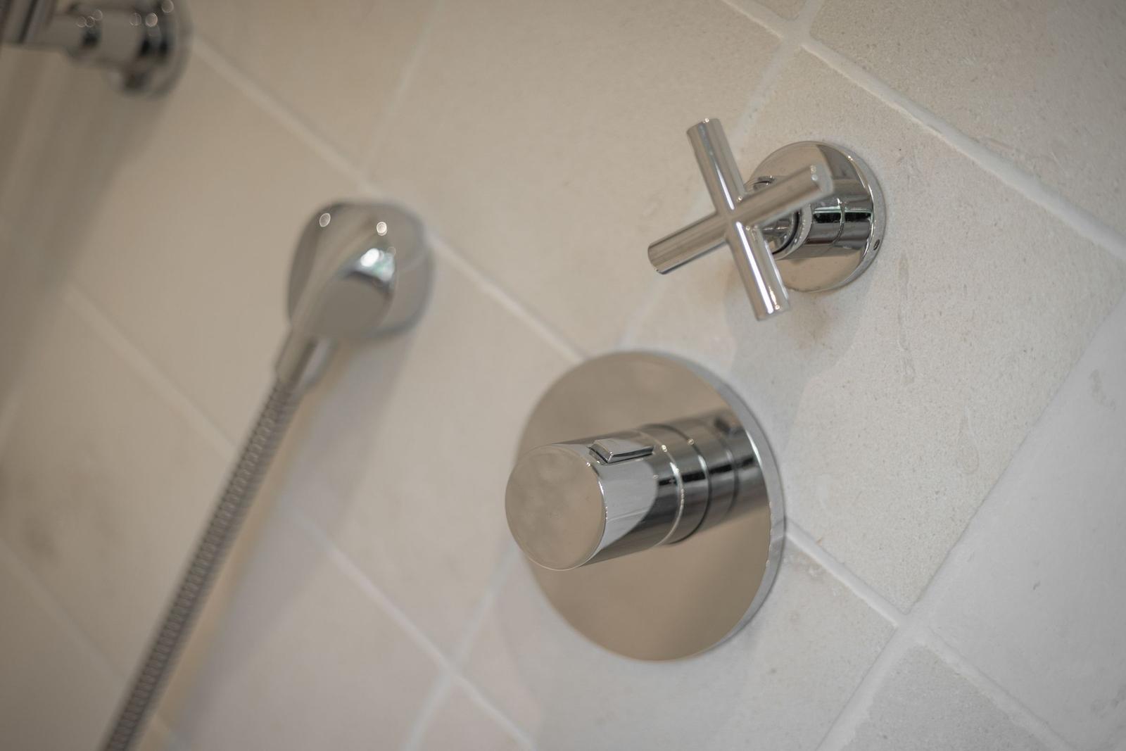 Shower head and controls mounted on tiled wall.