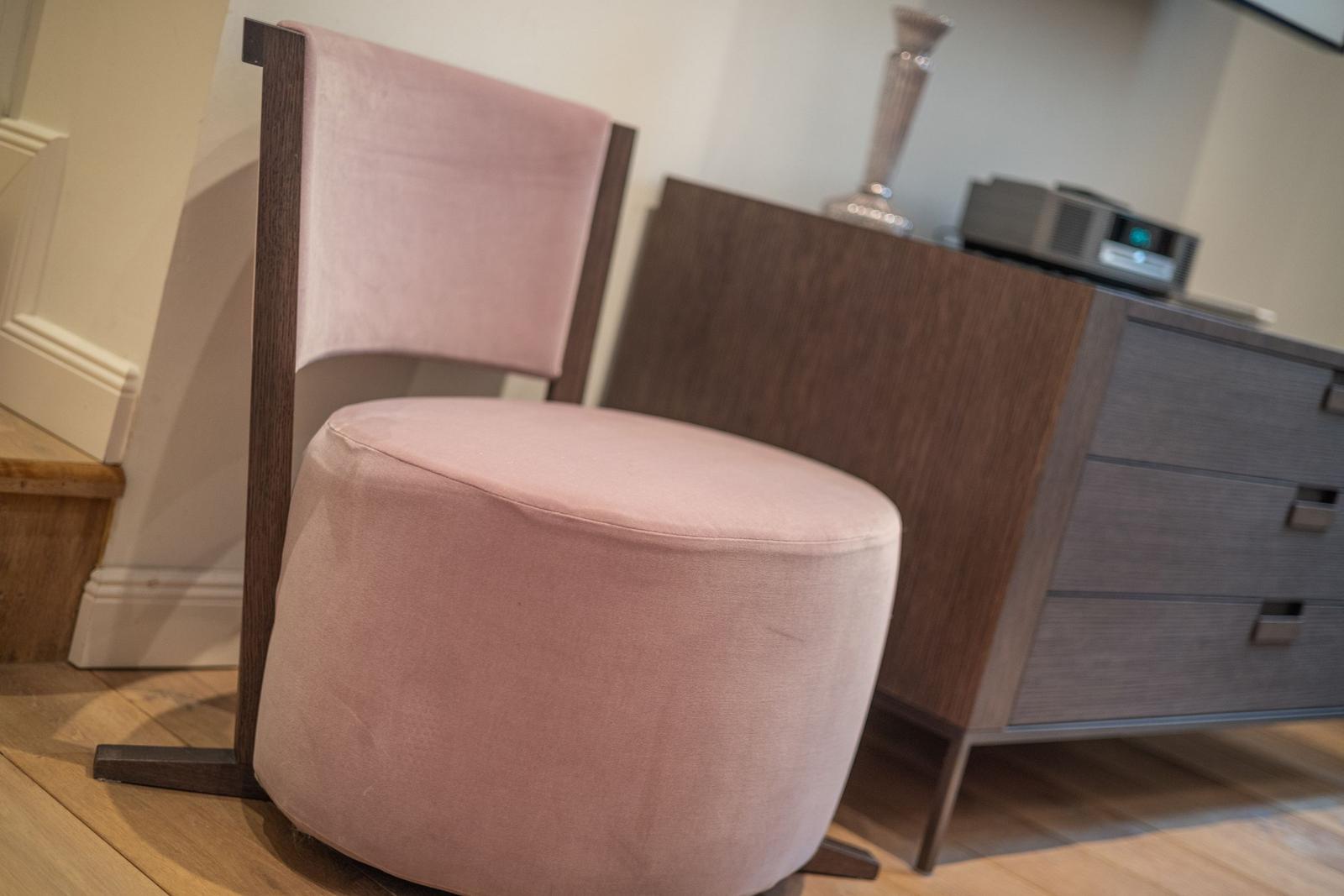 A pink seating area with wooden frame stands in front of a cabinet.