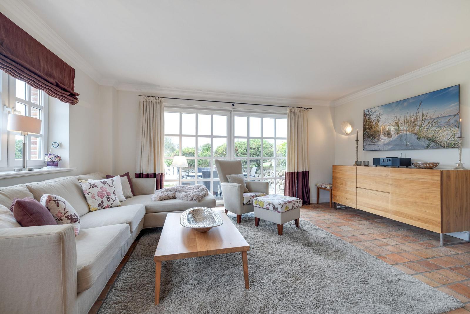 Living room with sofa, armchair, and coffee table. Windows overlook the garden.