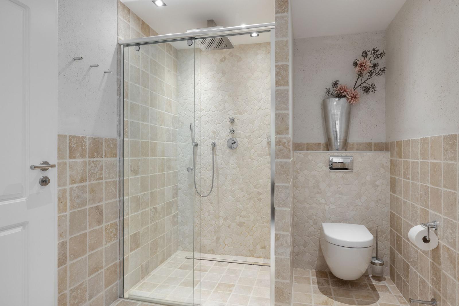 Shower with glass enclosure, toilet, and wall decor with flowers.