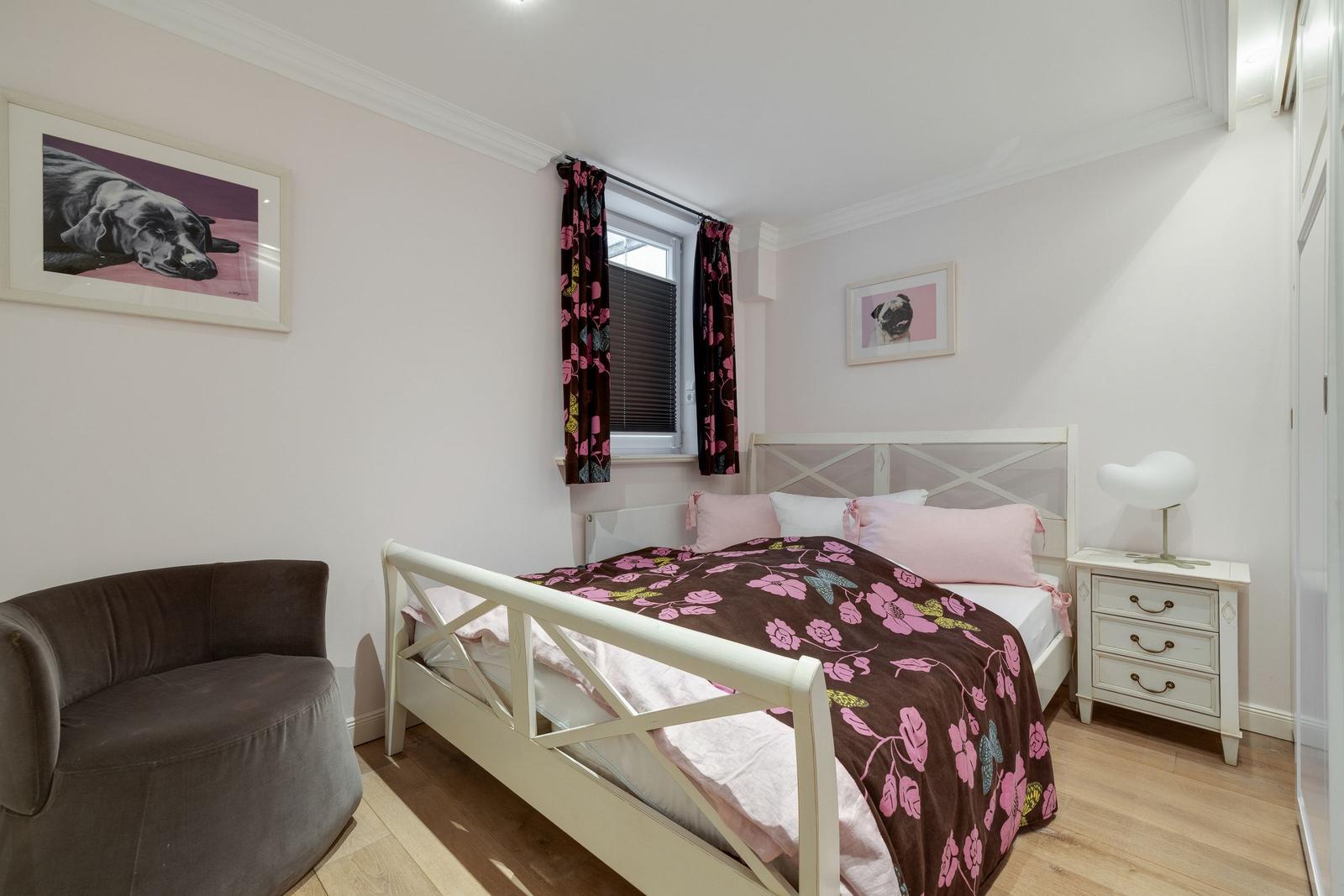 Bedroom with white bed, brown chair, and wall pictures of dogs.