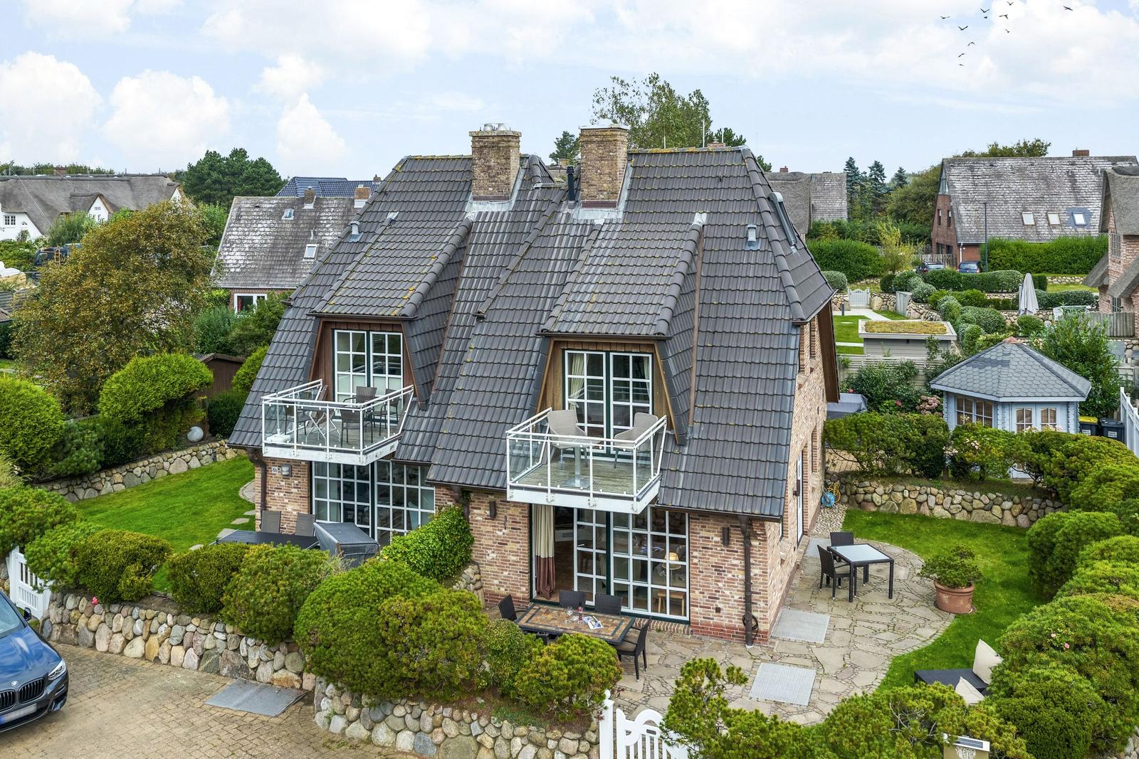 House with balconies, garden and stone walls. Terrace with table and chairs.