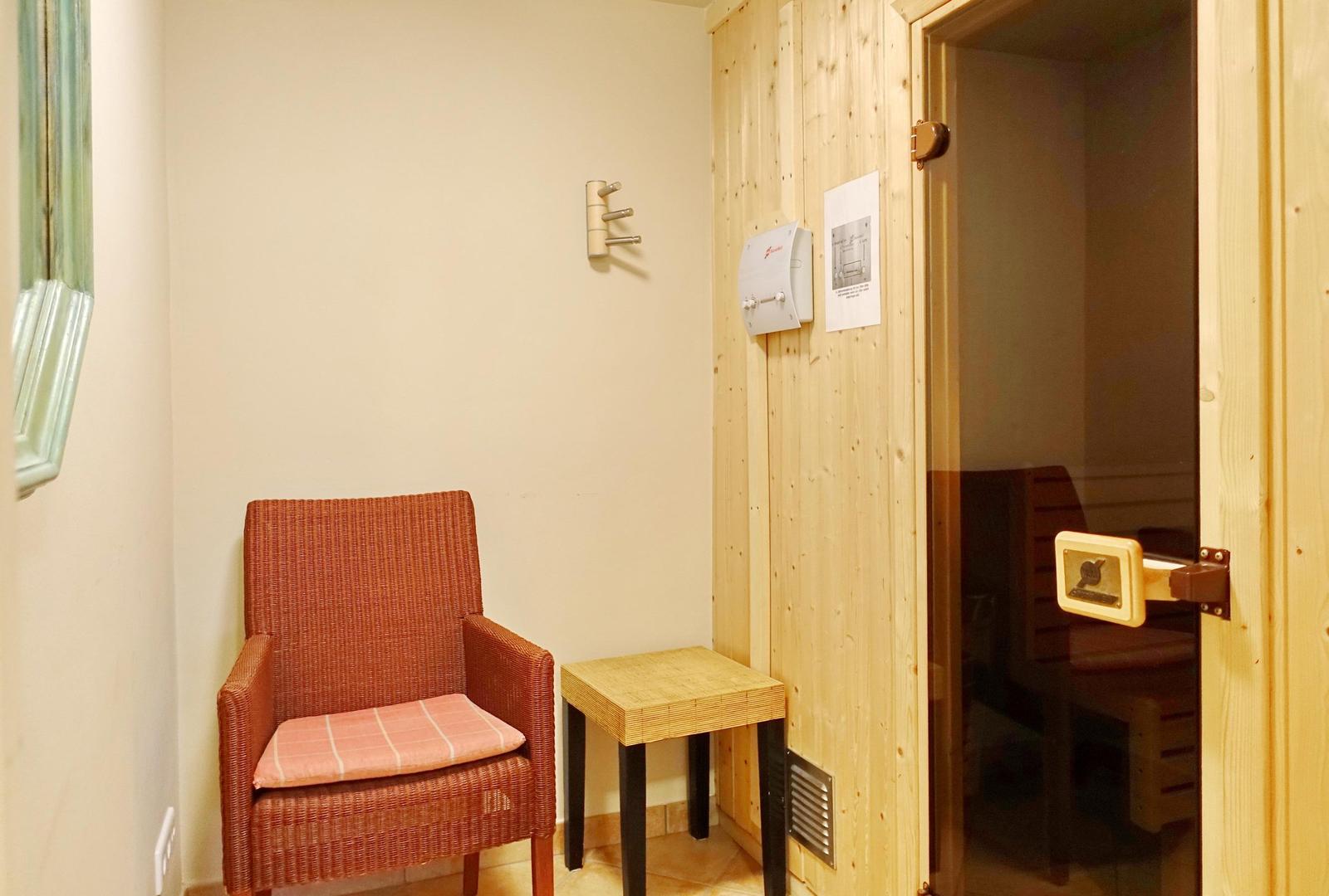 Sauna mit Holzwand und Stuhl. Draußen ein Sitzplatz mit Kissen.