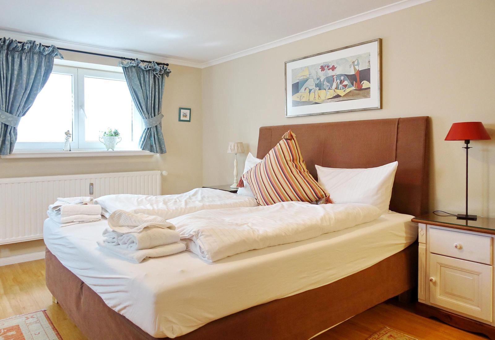 Schlafzimmer mit Bett, Nachttisch und Fenster mit Vorhängen.