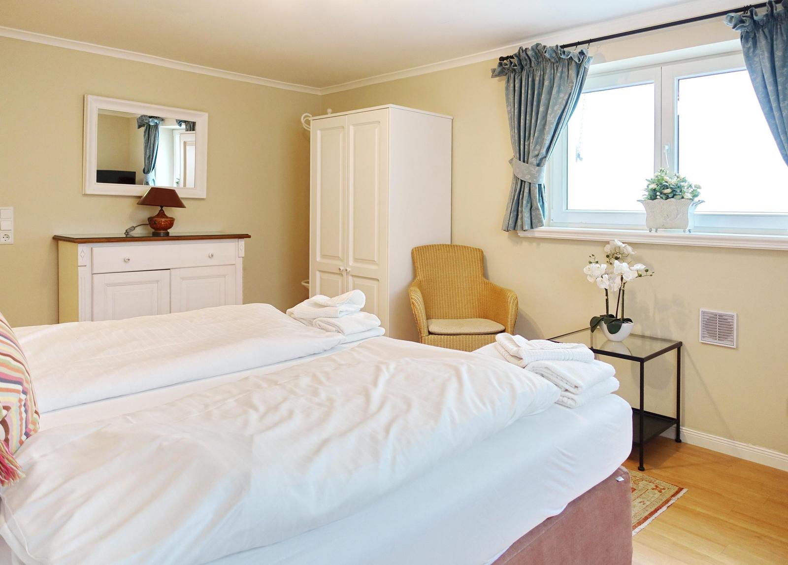 Schlafzimmer mit Bett, Schrank, Stuhl und Fenster mit Vorhängen.