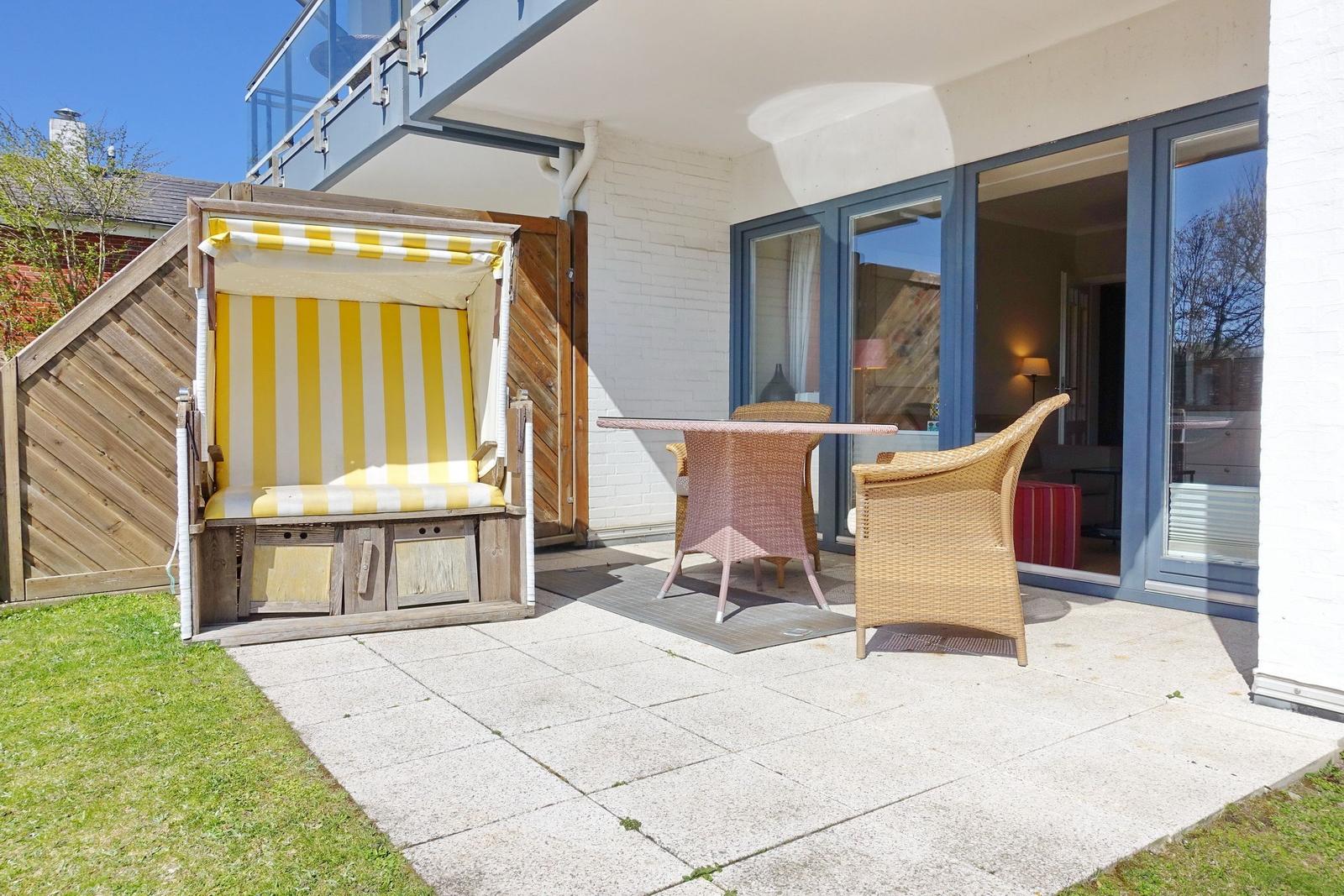 Terrasse mit Strandkorb und Sitzgruppe vor Glasfront.