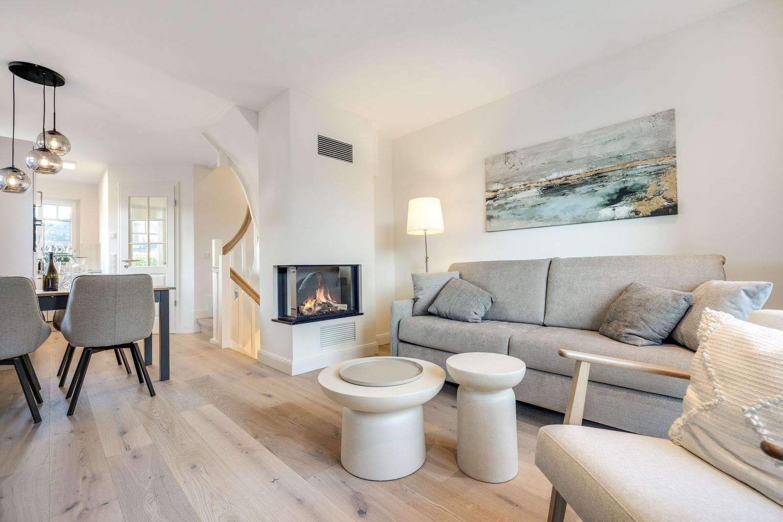 Living room with sofa, fireplace, and dining area. Wooden floor and modern furnishings.