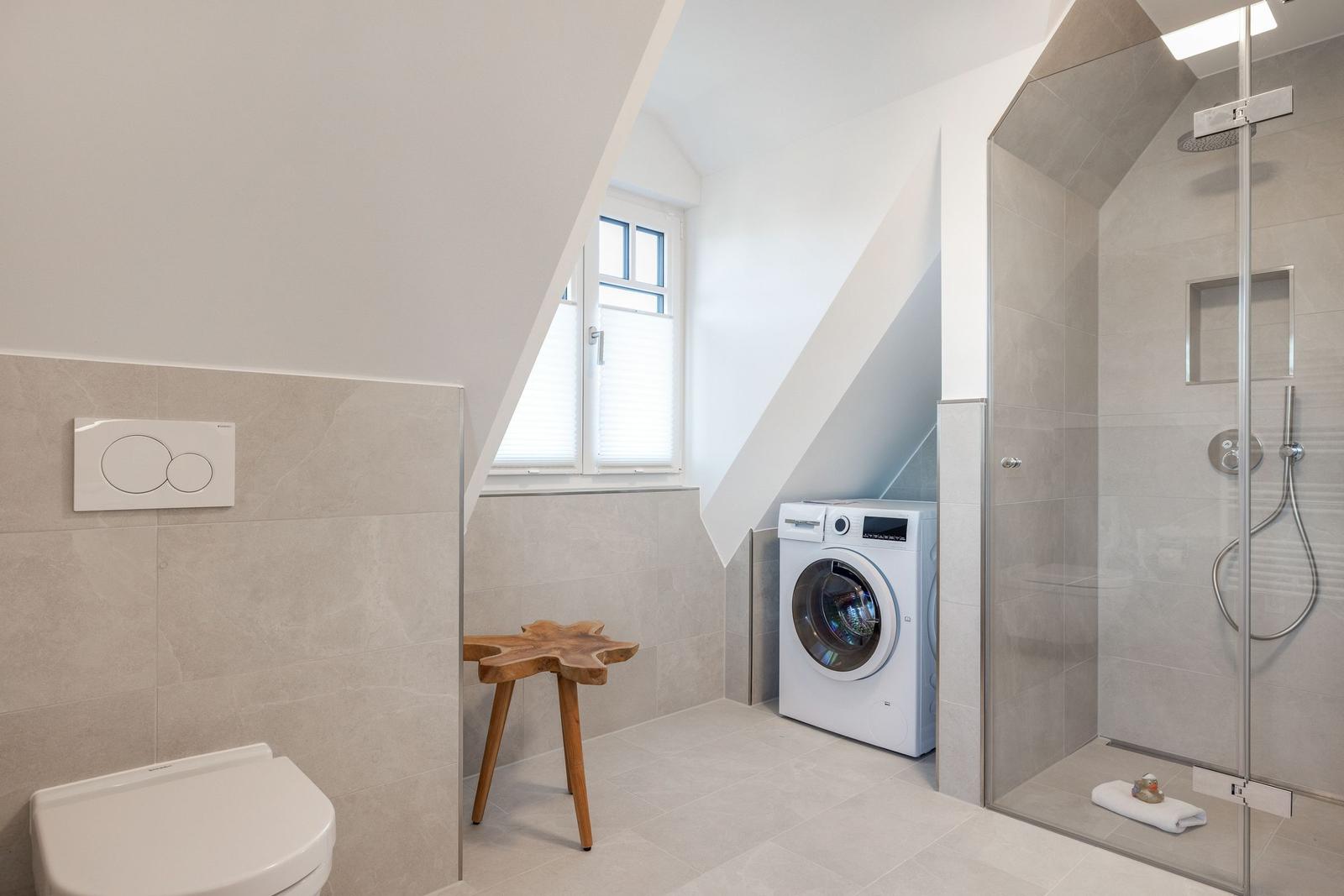 Bathroom with shower, washing machine, and toilet under sloped ceilings.