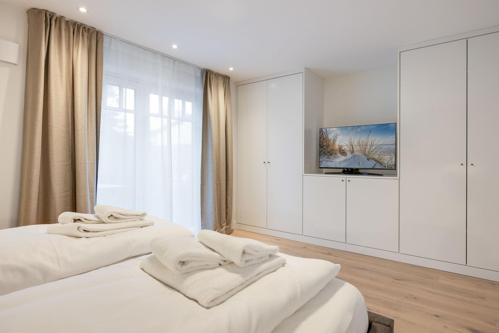 Bedroom with bed, TV, and cabinets. Window with curtains.