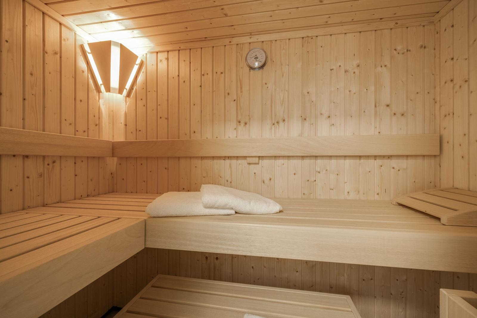 Wooden sauna with multiple benches and a thermometer on the wall.