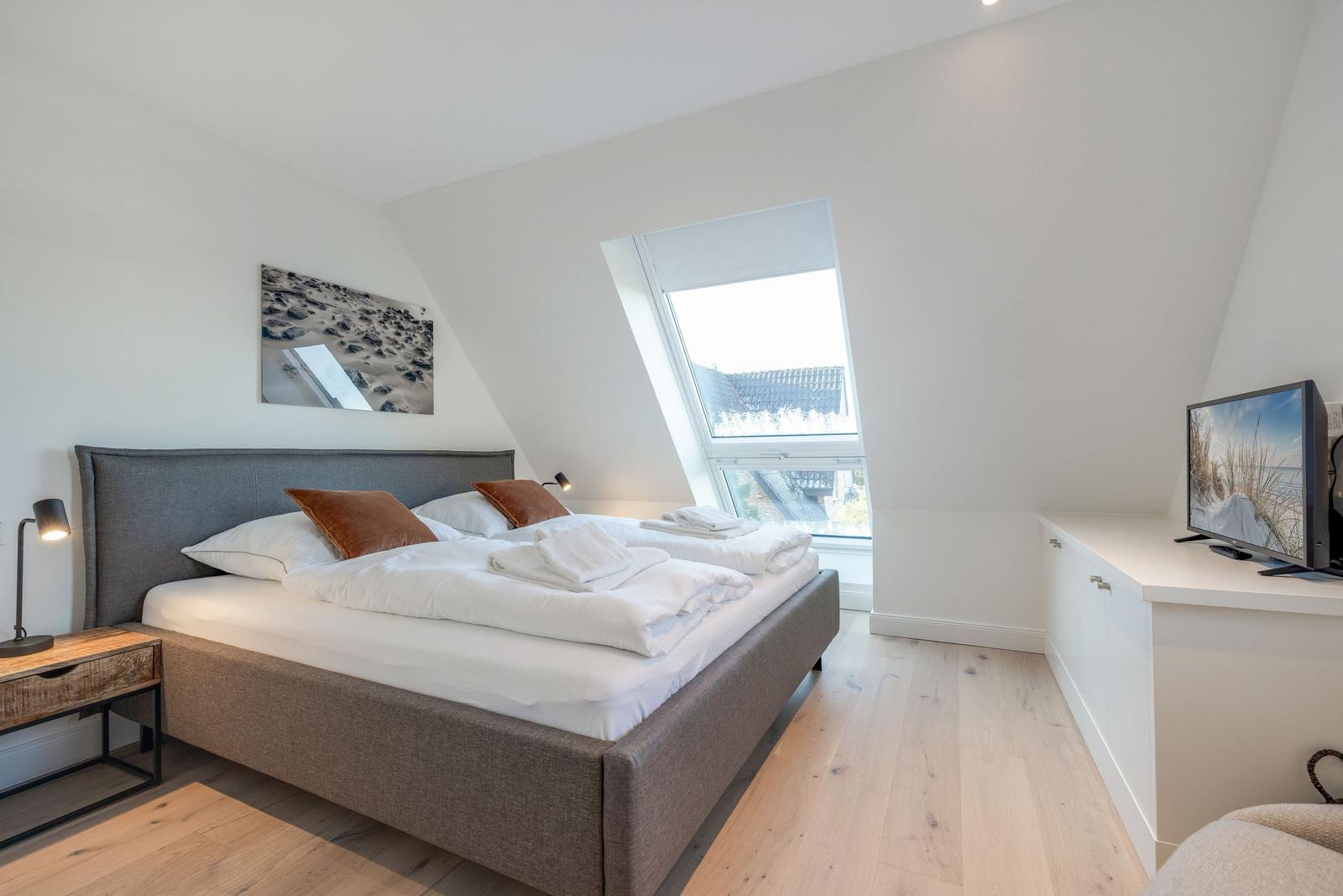 Bedroom with skylight, bed, nightstand, and TV.