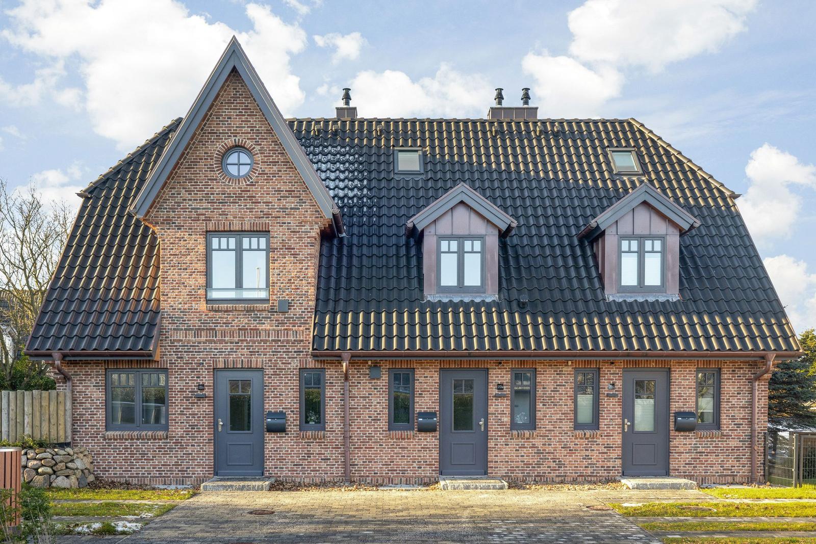 Two-family house with brick facade and dormers. Three entrances and dark windows.