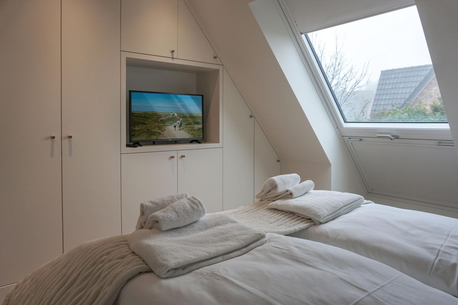 Zimmer mit Dachfenster, Bett und TV in Einbauschränken.