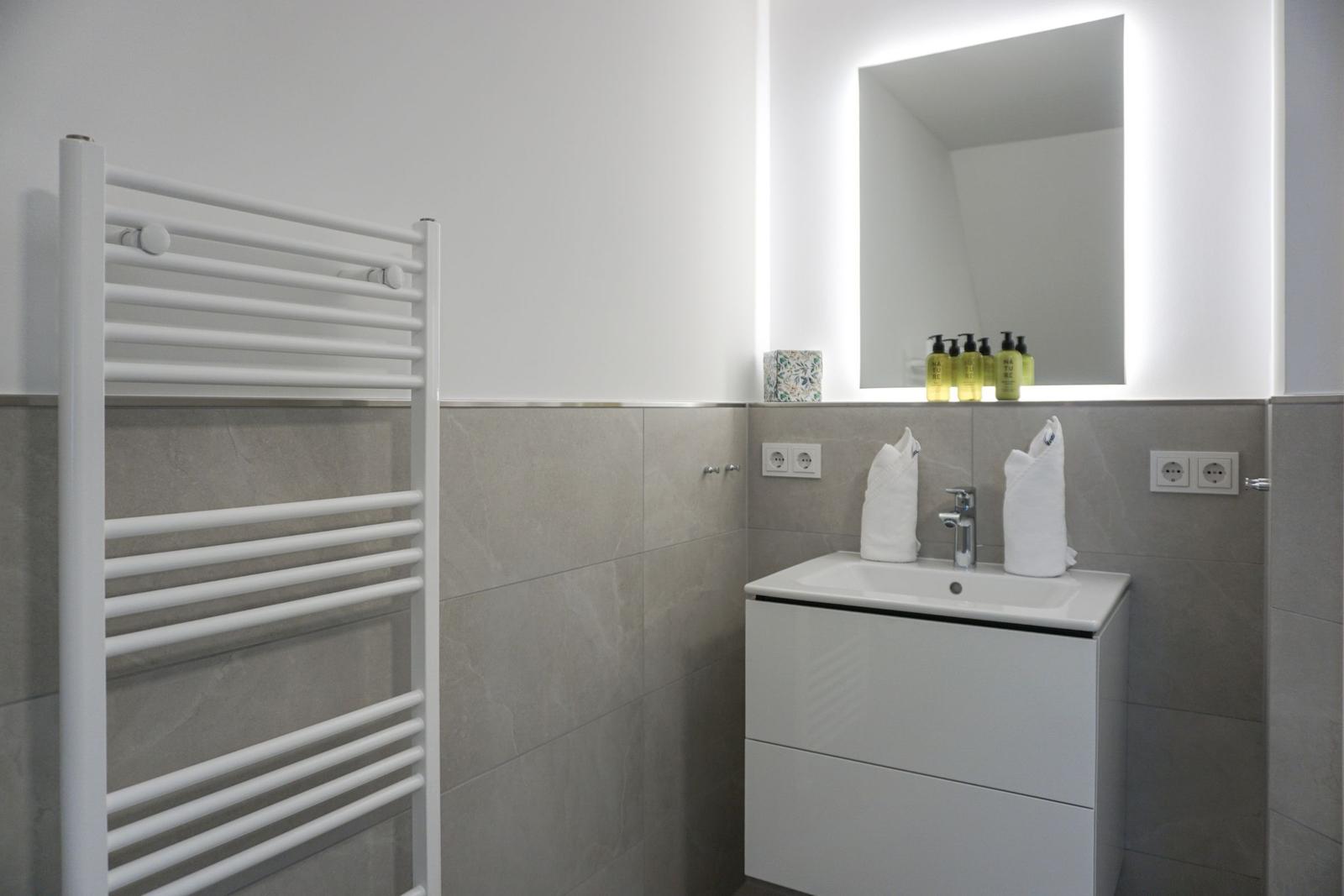 Badezimmer mit Waschbecken, Spiegel und Handtuchhalter.