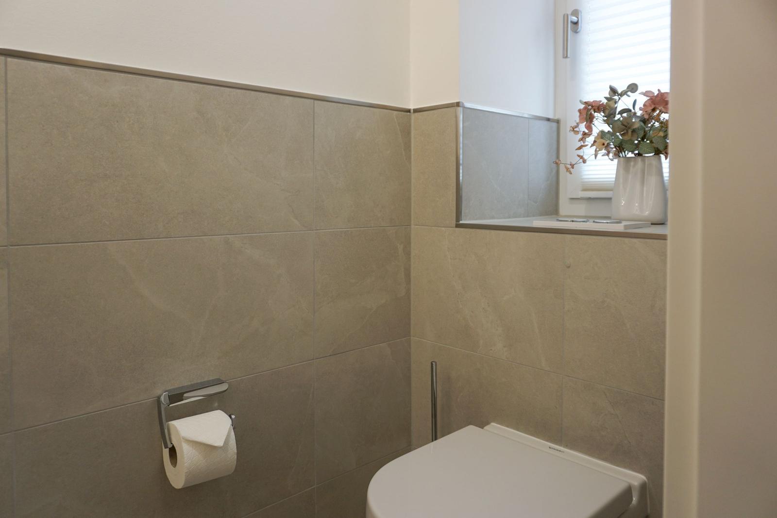 Bad mit Toilette, Toilettenpapierhalter und Blumen auf Fensterbank.