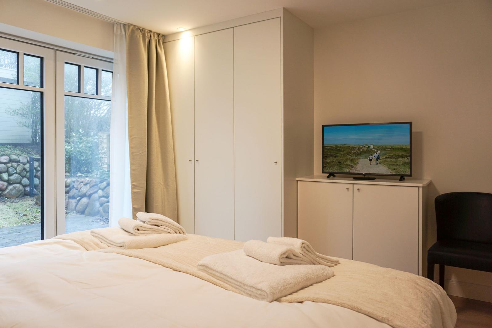 Schlafzimmer mit Bett, TV und Fenster zum Garten