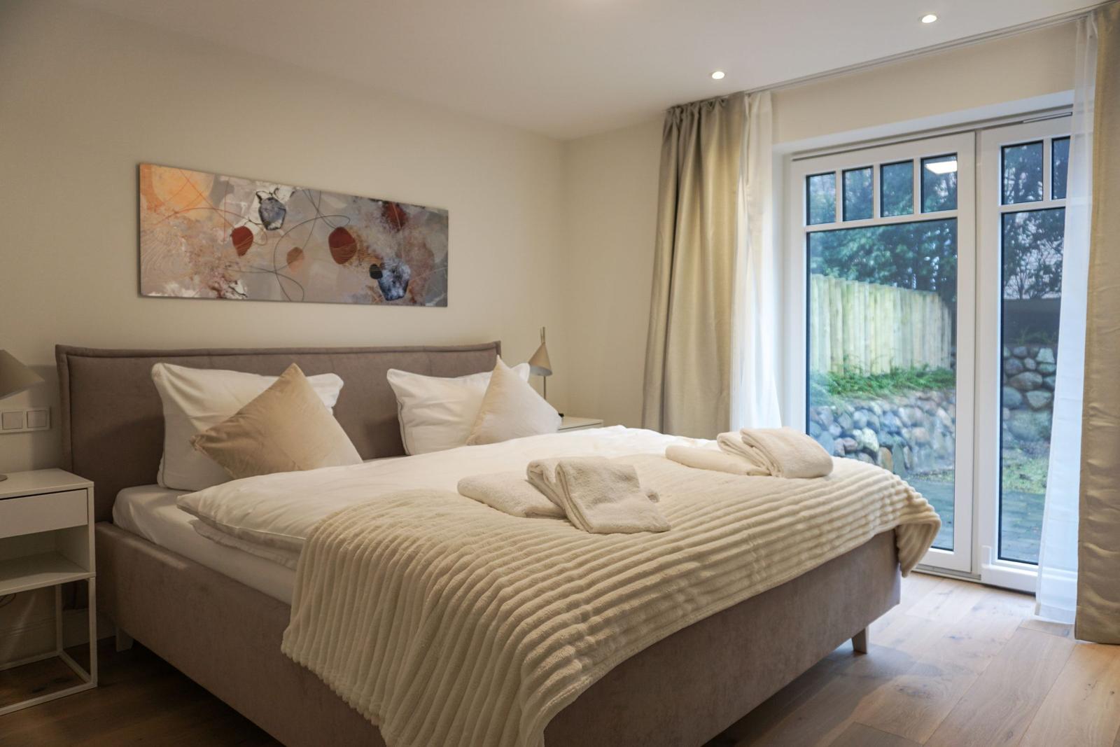 Schlafzimmer mit Doppelbett, Wandbild und Glastür zum Garten.